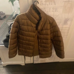 Brun pufferjacka från MNG, storlek M - Säljer en brun pufferjacka från MNG i storlek M. Jackan har en cool quiltad look, hög krage och knäppning framtill. 