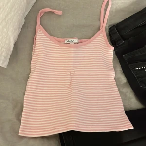 Rosa och vit randig linnetopp Subdued XS - Supersöt randig linnetopp från Subdued i storlek XS. Toppen är ljusrosa och vit med smala axelband och croppad passform. Materialet är mjukt ribbad bomull som sitter skönt mot kroppen. Perfekt för varma dagar och chill outfits!