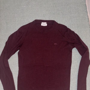 Vinröd merinoullströja Lindbergh - Vinröd långärmad tröja från Lindbergh. tillverkad i  merinoull. Klassisk rund hals och diskret logga på bröstet. Perfekt för dig som gillar stilrena och bekväma plagg med lite lyxig känsla.