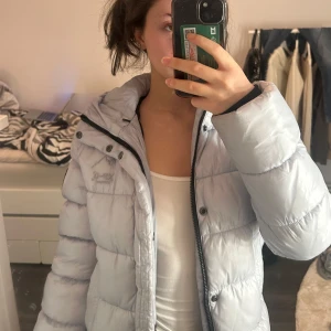 Ljusblå pufferjacka med huva - Säljer min ljusblå pufferjacka från Superdry. Älskar denna, perfekt för vintern då den håller super varm. Slusåld på nätet. 36, men passar som 34 också.  Pris går o diskutera. Kontakta vid intresse 🤍                                                                                                                                                                              Endast en lite smink på fickan/ går säkert att få bort