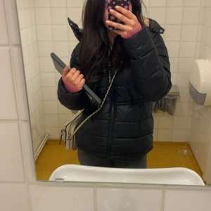 Svart pufferjacka  - Säljer en svart pufferjacka med luva och dragkedja. Perfekt för kalla dagar och riktigt skön att bära. Logga på ärmen och snygg, enkel design.