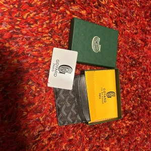 Svart  plånbok med mönster - Snygg och stilren svart plånbok  med ikoniskt grafiskt mönster i vitt. Plånboken är tunn och smidig, perfekt för kort och sedlar. Kommer med original ask och gul putsduk. Lyxig detalj för dig som gillar exklusiva accessoarer.