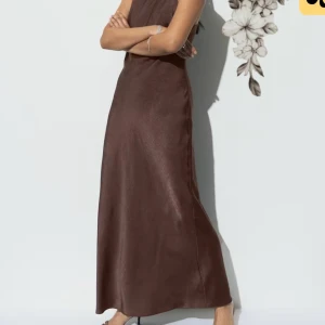 Brun långklänning från Gina Tricot - Supersnygg brun långklänning från Gina Tricot i storlek 38. Klänningen har en slät, lätt glansig yta och är ärmlös med smala axelband. Den har en rak, elegant siluett och är perfekt för dig som gillar minimalistisk stil med en touch av lyx.
