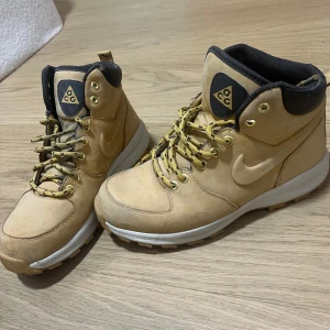 Nike ACG boots i beige mocka - Säljer ett par snygga Nike ACG boots i beige mocka med svart vadderad kant och robust snörning med guldfärgade öljetter. Skorna har en vit platt sula med grovt mönster för extra grepp. Perfekta för dig som gillar outdoor och streetstyle. Perfekta till vintern!