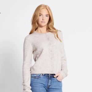 Beige stickad kofta med knappar - Supermjuk och stilren beige stickad kofta med rund hals och knäppning framtill. Långärmad modell i en ljus ton, perfekt att slänga över en t-shirt eller linne. Enkel och clean design som funkar till jeans eller kjol. Har haft på mig ett par gånger ser och känns helt ny ut. 