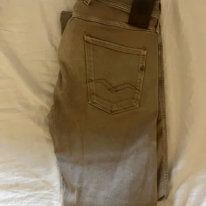 Beige Replay Anbass jeans, stl 32/30 - Säljer ett par snygga Replay Anbass jeans i beige färg. Modellen har klassisk femficksdesign, raka ben och diskreta sömmar på bakfickan. Jeansen är tillverkade i mjukt bomullsmaterial med en skön passform. Perfekta för dig som gillar stilrena och bekväma jeans.