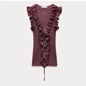 Vinröd volangtopp från Zara - Supersöt vinröd topp från Zara med volanger längs ärmhål och hela framsidan. Djup v-ringning och knyt framtill ger en unik look. Stickad känsla och ärmlös design.