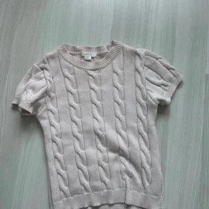 Ljus rosa stickad tröja Gina Tricot - Snygg ljus rosa stickad tröja från Gina Tricot med korta ärmar och klassiskt kabelstickat mönster. Rund halsringning och ribbade muddar vid ärmslut och nederkant. Perfekt för dig som gillar en clean och chill stil.