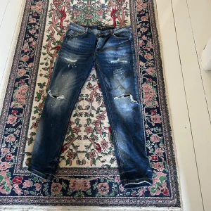 Blå slitna jeans med skinny fit - Säljer ett par blå jeans från supply and demand med lite baggy passform och coola slitningar samt hål på knäna. Jeansen har klassisk femficksdesign, dragkedja och knapp i midjan. 