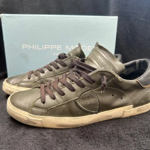 Philippe Model gröna skor - Snygga sneakers från Philippe Model i mörkgrönt skinn med svarta snören och beige sula. Klassisk låg modell med rund tå och diskret logga på sidan. Perfekta för dig som gillar stilrena och exklusiva sneakers med en urban vibe.