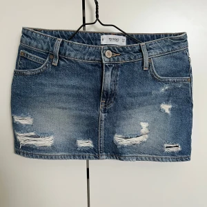 Blå jeanskjol Mango - Snygg blå jeanskjol från Mango med slitna detaljer och klassisk femficksdesign. Kjolen har en knapp och dragkedja framtill💘