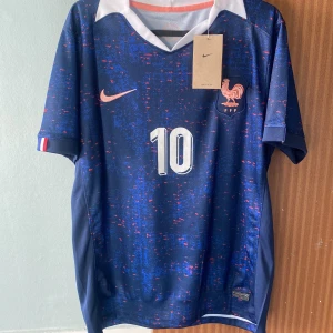 Frankrike Mbappé #10 Nike fotbollströja S - Frankrikes landslagströja från Nike med Mbappé och nummer 10. Djupblå bas med röda och blå detaljer, vitt nummer och namn, samt FFF-emblem på bröstet. Kortärmad modell i lätt funktionsmaterial, perfekt för fotboll eller supporterliv.