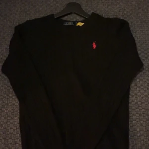 Svart stickad tröja Polo Ralph Lauren - Svart stickad tröja från Polo Ralph Lauren med klassisk röd broderad logga på bröstet. Tröjan har rund halsringning och ribbade muddar. Perfekt för dig som gillar stilrena och tidlösa plagg. Pris kan diskuteras!
