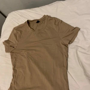 Beige basic t-shirt i bomull - Enkel och stilren beige t-shirt med rund halsringning och korta ärmar. T-shirten är i mjuk bomull och har en klassisk passform som funkar till det mesta. Perfekt för dig som gillar en clean och neutral look.