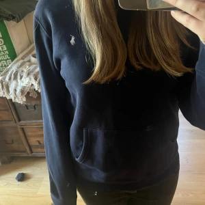 Mörkblå hoodie från Polo Ralph Lauren - Säljer en mörkblå hoodie från Polo Ralph Lauren med klassisk broderad logga på bröstet. Tröjan har magficka, långa ärmar och är tillverkad i mjuk bomullsmix. Perfekt för chill dagar eller när du vill ha en stilren look. är XL men i barn storlek passar som small