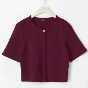 Vinröd croppad blus med knapp - Säljer en vinröd croppad blus från GU med korta ärmar och rund halsringning. Toppen har en snygg guldig knapp framtill som detalj och är enkel men stilren. Perfekt att matcha med höga jeans eller kjol.