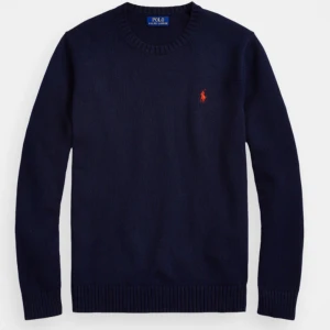 Mörkblå  Polo Ralph Lauren tröja - Mörkblå stickad tröja från Polo Ralph Lauren med rund halsringning och klassisk röd logga broderad på bröstet. Tröjan har långa ärmar och ribbade muddar vid ärmslut och nederkant. Perfekt för dig som gillar stilren och tidlös design. Den är i väldigt bra skick knappt använd!