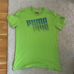 Grön Puma t-shirt bra condition och kvalité - Snygg grön t-shirt från Puma med blått tryck på bröstet där det står 'PUMA 1948'. Klassisk rund halsringning och korta ärmar. Tillverkad i mjuk bomull, perfekt för en avslappnad stil.