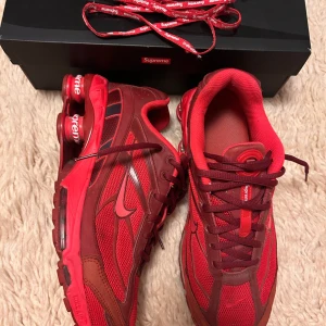 Nike x Supreme Shox TL röda sneakers - Nike Shox TL Supreme i helrött med Supreme-detaljer på sulan och skosnören. Skorna har mesh och syntetpaneler, klassisk snörning och den ikoniska Shox-dämpningen. Perfekta för dig som vill sticka ut med en unik och limiterad sneaker.