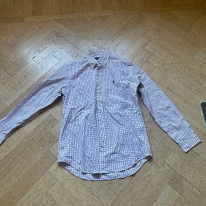 Rutig skjorta från Polo Ralph Lauren - Klassisk rutig skjorta från Polo Ralph Lauren i vitt med blått och rött rutmönster. Skjortan har lång ärm, knappar framtill och broderad logga på bröstet. Tillverkad i mjuk bomull och har en normal passform. Perfekt för en clean och stilren look.