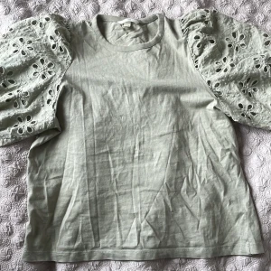 Ljusgrön blus med broderade puffärmar H&M - Superfin ljusgrön blus från H&M med broderade puffärmar i bomull. Ärmarna har snygga hålbroderier i blommönster som ger en unik look. Rak passform och rund halsringning. Perfekt för dig som vill ha något extra till din outfit. Den på bilden är i storlek M men säljer i xs.