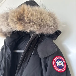 Svart dunjacka från Canada Goose - Säljer en svart dunjacka från Canada Goose med ikonisk patch på ärmen och stor huva med fluffig päls. Jackan har dragkedja framtill, långa ärmar och en klassisk pufferlook som håller dig varm hela vintern. Perfekt för kalla dagar och snygg till allt. Storlek: står xxs men passar mig som är xs-s. Pris går absolut att diskutera! Nypris runt 15000kr