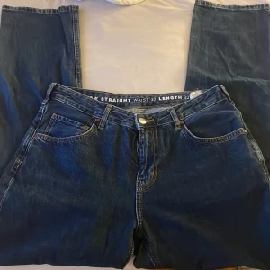 Mörkblå straight jeans midwaist 32/32 - Snygga mörkblå jeans med raka ben. Midjan är midwaist och passformen är straight. Jeansen har kontrastsömmar och stängs med knapp och dragkedja. Perfekta för en clean och tidlös look.