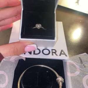 Pandora silverring och armband - Säljer ett set från Pandora med en glittrig silverring med hjärtformad sten och ett klassiskt silverarmband. Perfekt för dig som gillar stilrena och eleganta smycken med det lilla extra. Kommer i originalask.700kr per st