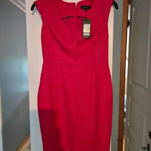 Röd klänning från New Look - Snygg röd klänning från New Look med figurnära passform och markerad midja. Klänningen har breda axelband, rundad halsringning och dragkedja bak. Materialet är strukturerat och känns bekvämt mot huden. Perfekt för dig som vill sticka ut med en färgstark look.