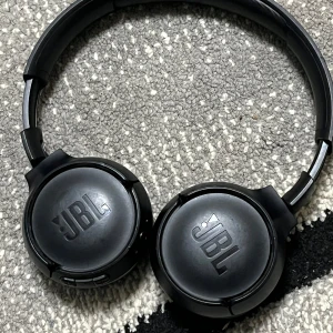 JBL trådlösa over-ear hörlurar - Snygga svarta JBL over-ear hörlurar med trådlös anslutning. Hörlurarna är i gott skick med mjuka öronkuddar och synliga knappar för enkel kontroll. Laddningsport och ljudingång finns. Perfekt för musik och samtal på språng. Har använt dom bara i 3 månader och vill gå av med dom perfekt för dom som sportar eller springer på kvällarna.