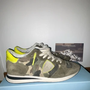 Philippe Model sneakers camo & neon - Snygga sneakers från Philippe Model med camouflage-mönster i grönt och beige, detaljer i mocka och coola neon-gula inslag på häl och snörhål. Skorna har vit sula med svart rand och klassisk snörning. Perfekta för dig som vill sticka ut med streetstyle-vibe.