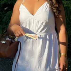 Vit sommarklänning från Bik Bok - Superfin vit kortklänning från Bik Bok med smala axelband som korsas i ryggen. Klänningen har v-ringning och markerad midja, perfekt för varma dagar. Tillverkad i mjuk bomull som känns lätt och luftig. Enkel och stilren design som ger en fräsch look.