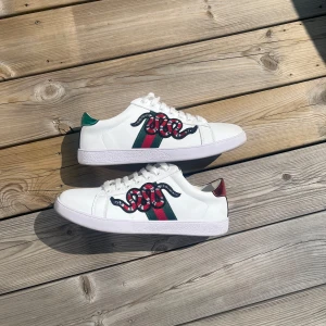 Gucci Ace snake  - använda 1 gång, Gucci Ace sneakers i vitt skinn med klassiska gröna och röda ränder på sidorna och broderad orm. Baksidan har metallicdetaljer i grönt och rött med Gucci-logga. Snygg och ikonisk modell som sticker ut med sina detaljer.