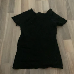 Svart smockad topp från H&M - Svart smockad topp från H&M med korta ärmar och stretchig passform. Toppen har en lätt rynkad struktur och volangkant vid halsringning och ärmslut. Perfekt att styla med jeans eller kjol för en cool och enkel look.