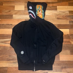 Svart BAPE Shark Hoodie storlek M - Säljer min svarta Bape Shark hoodie i storlek M men passar bättre med dom som har S. Ni som har M det kommer sitta ganska tajt på er.