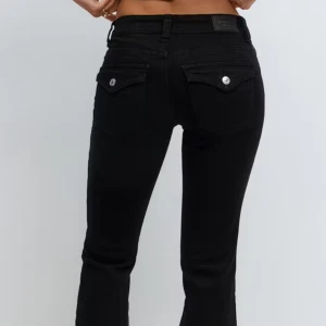Low y2k jeans - Svarta jeansbyxor från gina med klassisk femficksdesign och snygga ficklock med silverknappar bak. Byxorna har en bootcut passform och är tillverkade i mjukt jeanstyg med stretch för extra komfort. Perfekta för en stilren och enkel look. Jeansen är nedtagna nertill och är bra l längd för någon runt 165/170