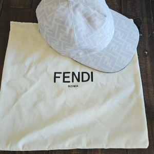 Vit keps från Fendi med logomönster - Snygg vit keps från Fendi med det klassiska FF-logomönstret över hela kepsen. Stilren design med böjd skärm och justerbar passform. Perfekt för dig som vill ha en exklusiv och trendig accessoar från ett lyxigt italienskt märke.
