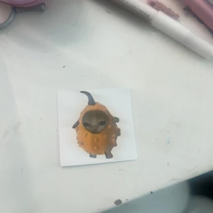 Sticker  - Bilderna visar en fyrkantig klistermärke med en tecknad figur av ett djur i en orange dräkt, troligen en dekorativ sticker. Ingen elektronikprodukt syns på bilderna.