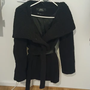 Köp - Mysig svart teddyjacka från Viva Couture med bred krage och knytskärp i midjan. Jackan har lång ärm och är tillverkad i ett fluffigt teddy-material som ger en cool och trendig look. Perfekt för dig som vill ha en varm och snygg jacka till hösten och vintern. Har använt den bara en gång 