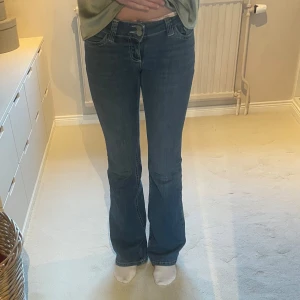 Blå bootcut jeans från Nelly med vit detalj på fickorna  - Snygga blå jeans från Nelly med bootcut-modell och klassisk femficksdesign. Jeansen har låg midja. De är i storlek 32.. Det är de populära byxorna från Nelly men som tyvärr inte kommer till användning hos mig. De är i väldigt bra skick, inga anmärkningar!! Ordinarie pris 699