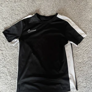 Svart och vit Nike Dri-Fit fotbollströja - Nike Dri-Fit fotbollströja i svart med vita paneler längs sidorna och axlarna. Klassisk rund hals och korta ärmar. Tillverkad i lätt och ventilerande funktionsmaterial som håller dig sval på planen. Swoosh-logga på bröstet.