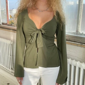 Olivgrön långärmad knytblus - Snygg olivgrön blus med djup v-ringning och knyt framtill. Långa ärmar med lätt utsvängd form och mjukt, tunt bomullstyg.