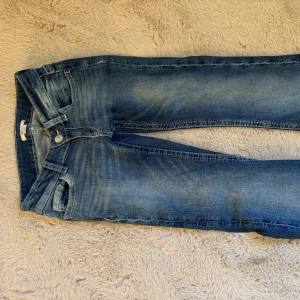 Blå jeans med broderad bakficka Gina Tricot - Snygga blå jeans från Gina Tricot i storlek XS. Jeansen har en klassisk femficksdesign och en bakficka med broderade detaljer och små pärlor. Materialet är stretchigt jeans och passformen är normal. Perfekta för dig som gillar unika detaljer på dina jeans.