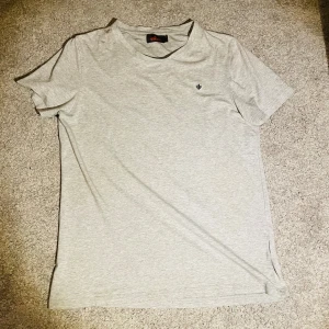 Morris tshirt - Ljusgrå t-shirt från Morris Stockholm i mjuk bomull. Klassisk passform med korta ärmar och rund hals. Liten broderad logga på bröstet ger en clean och stilren look. Perfekt till jeans eller shorts.