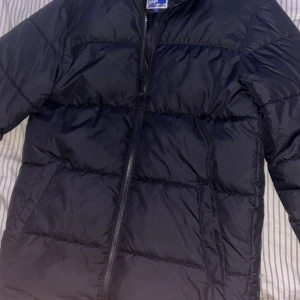 Svart pufferjacka från Jack & Jones - Säljer en svart pufferjacka från Jack & Jones. Jackan har quiltad design, dragkedja framtill och två sidofickor. Perfekt för kyliga dagar och har en stilren look som funkar till det mesta.Har använt två gånger typ. 