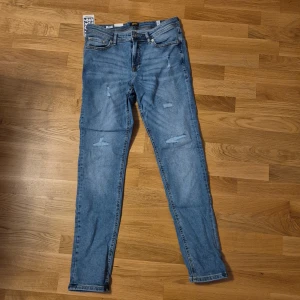 Jack & Jones Skinny Liam jeans blå - Säljer ett par ljusblå skinny jeans från Jack & Jones, modell Liam. Jeansen har klassisk femficksdesign, slitna detaljer framtill och smal passform hela vägen ner. Perfekt för dig som gillar en modern och tajt look.