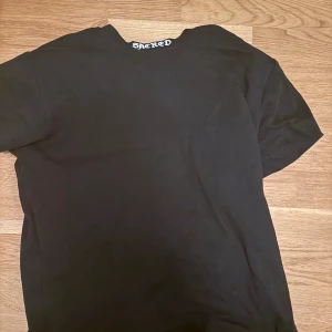 Svart t-shirt från Sacred - Svart t-shirt från Sacred med enkel design och rund halsringning. T-shirten har korta ärmar och tryckt logga i nacken. Perfekt basic-plagg i mjuk bomull som funkar till allt.