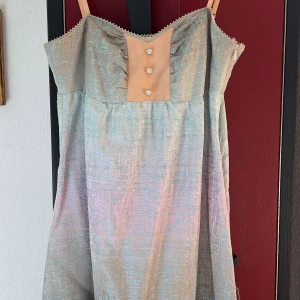 Prinsessig sidenklänning från Valerie - Superfin 100% sidenklänning från Valerie i skimrande gröns och rosa toner. Klänningen har smala axelband, dekorativa knappar framtill och spetskant upptill. 