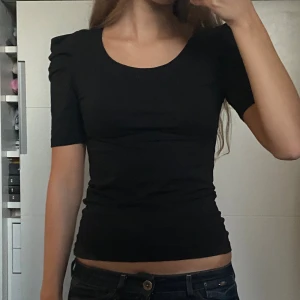 Svart topp med puffärm - Säljer en svart, tight topp med korta puffärmar och rund halsringning. Toppen har en tight passform och stretchigt material. Jättesnygg både till vardags och lite finare tillfällen! Den är från Vila i storlek xs. Nästan aldrig använd