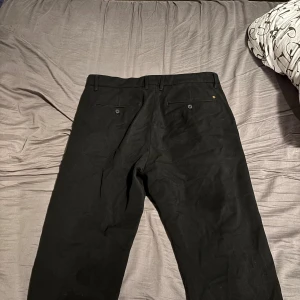 Svarta kostymbyxor från Gabba, L - Svarta kostymbyxor från Gabba i modellen Rome Pants. Byxorna har raka ben, bälteshällor och två bakfickor med knapp. Snygg och stilren design som passar till många olika outfits. Materialet känns mjukt och följsamt. Priset är diskuterbart!